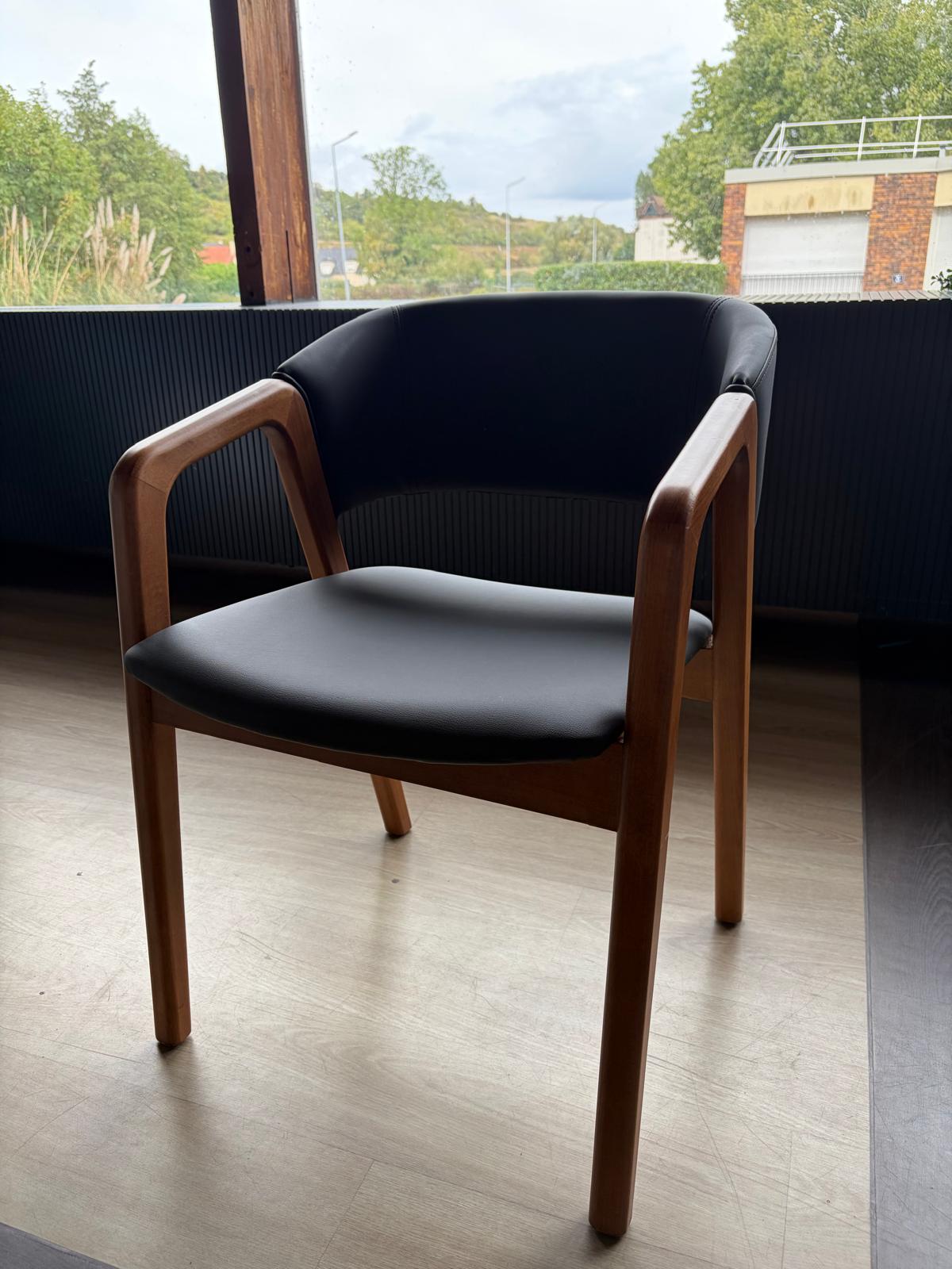 Chaise avec accoudoirs en bois clair et assise/dossier en simili cuir noir, vue de trois quarts près d'une fenêtre