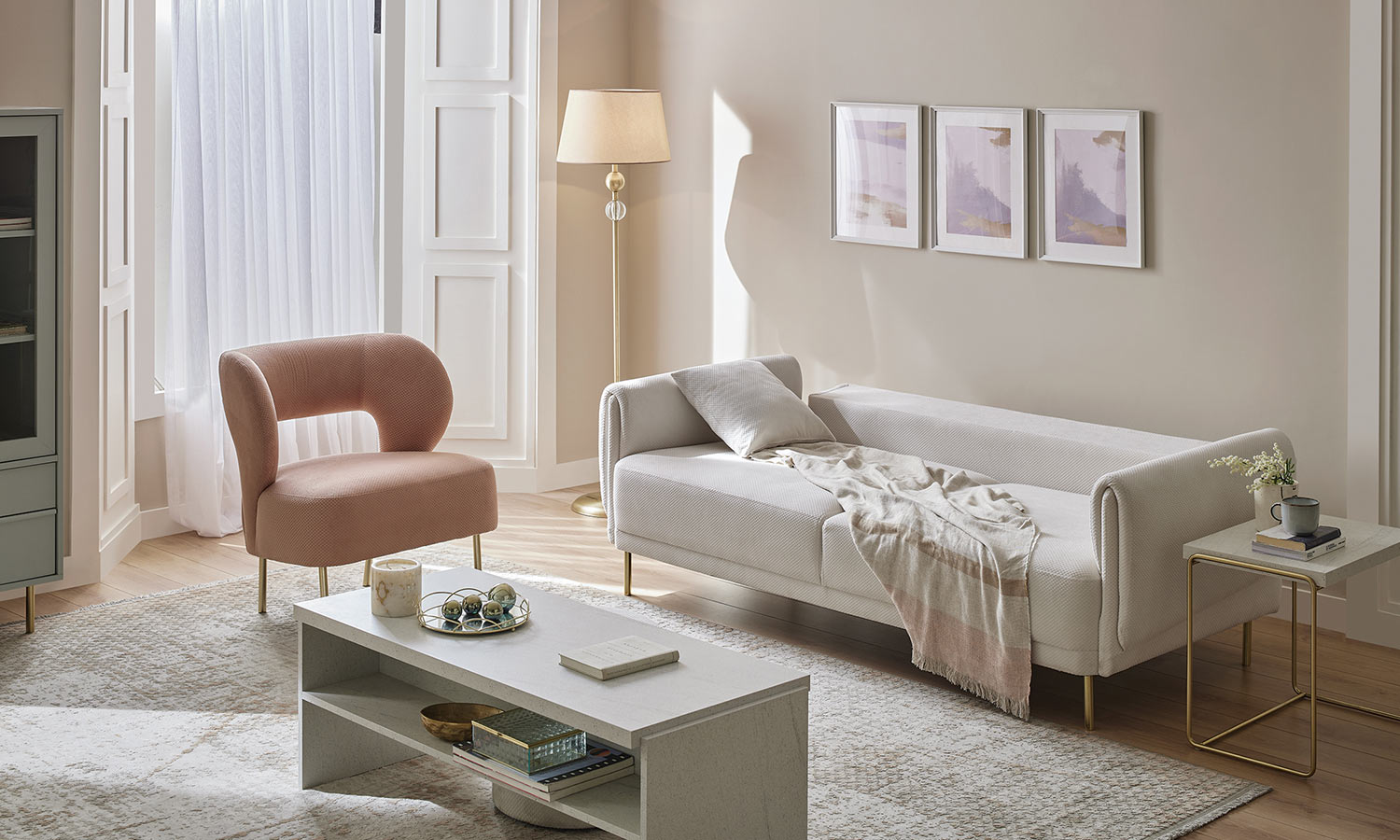 Canapé Karlin blanc cassé déplié en couchage avec plaid rose, fauteuil rose à côté, pieds dorés