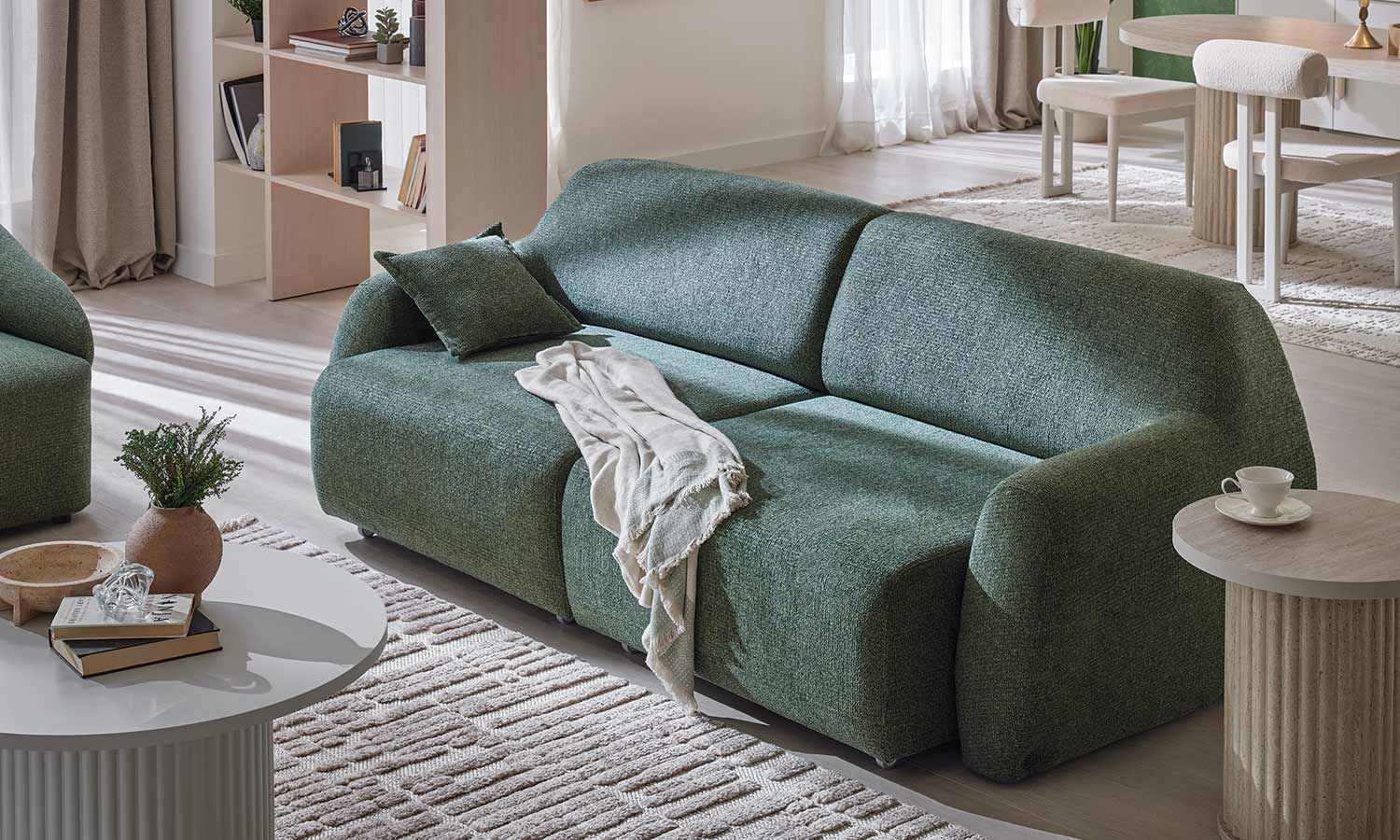 Canapé Latissa vert avec coussin déco et plaid blanc, vue rapprochée sur l'assise et l'accoudoir arrondi