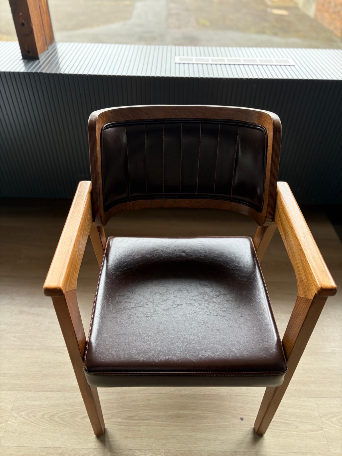 Chaise en bois avec dossier à cadre foncé et assise/dossier en simili cuir marron à surpiqûres verticales, vue de face