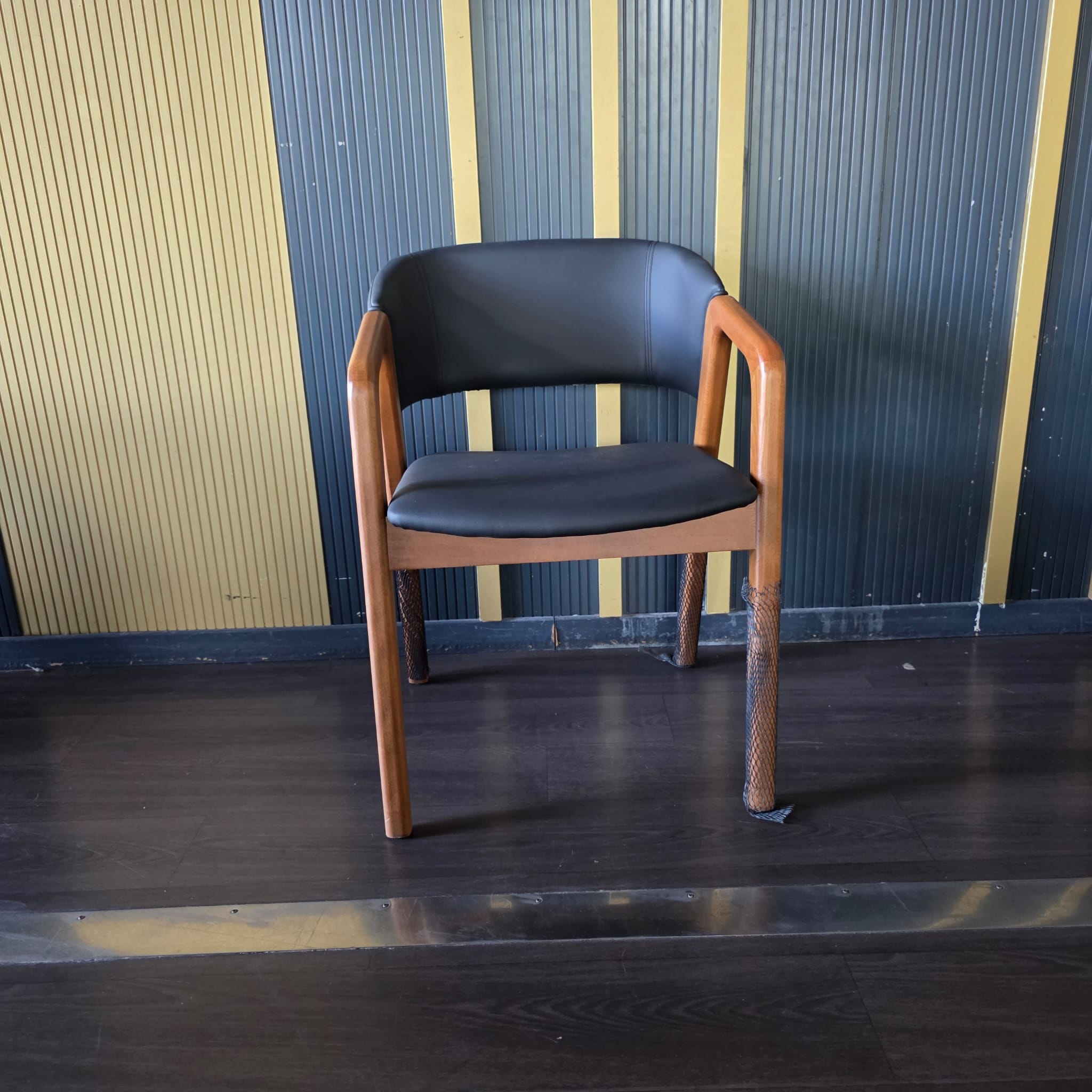 Chaise en bois avec accoudoirs et assise/dossier en simili cuir noir, pieds avant emballés pour transport